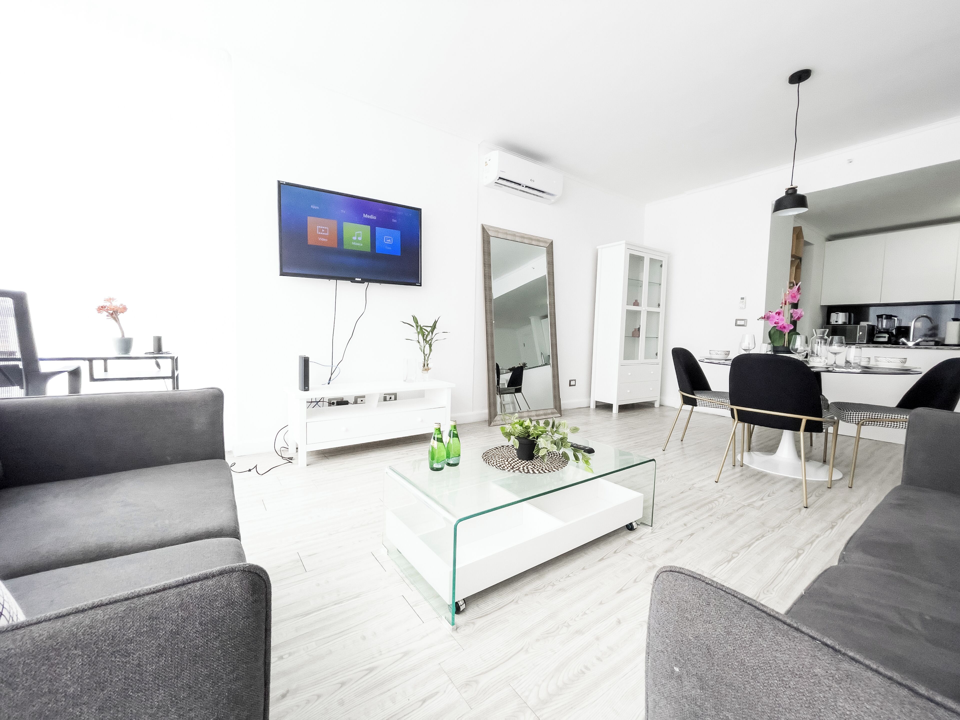 A modern living room with a flat-screen TV, a glass coffee table, and grey sofas.
