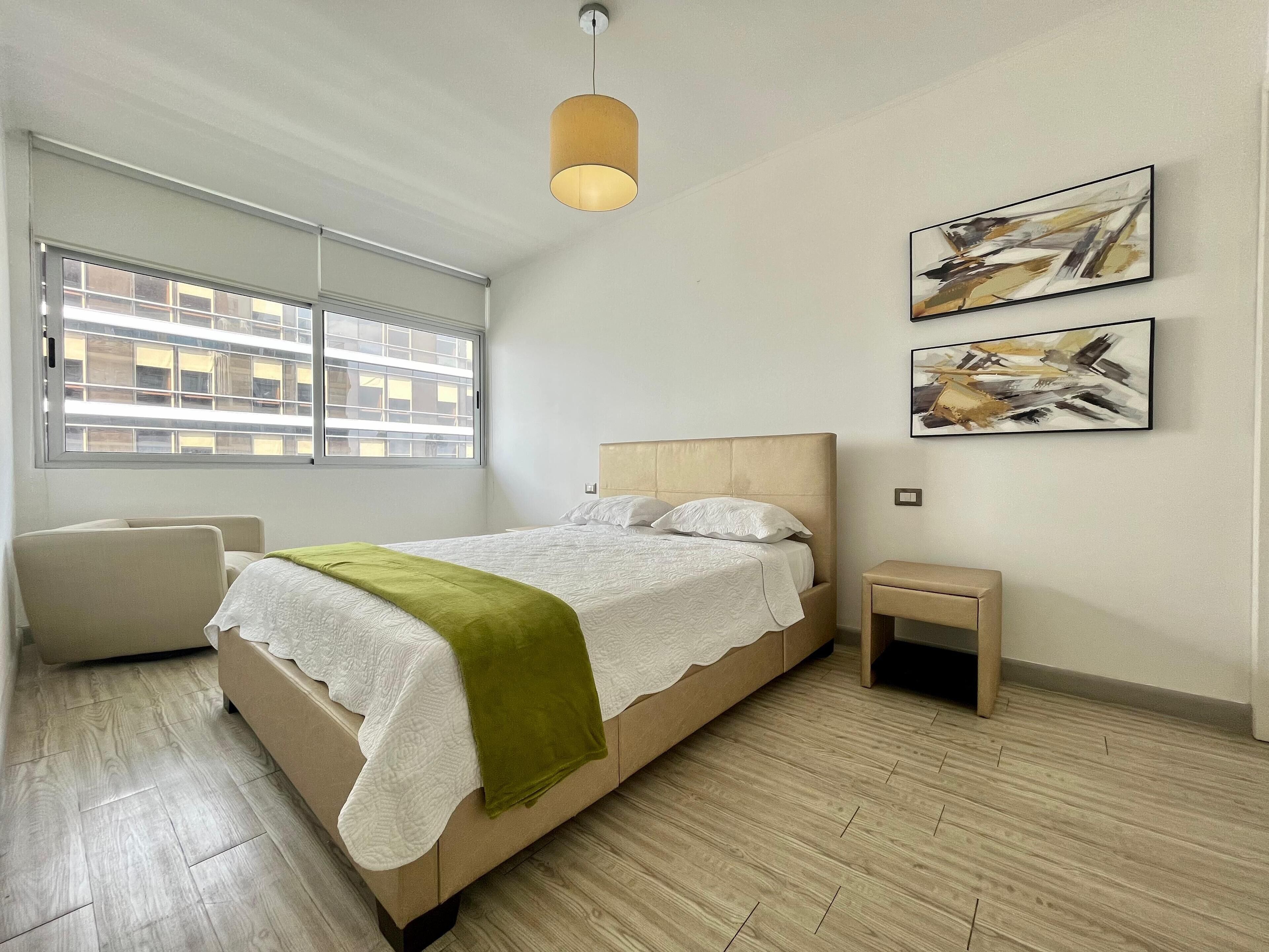 Camera da letto moderna con un letto, una sedia, un comodino e un'opera d'arte astratta sulla parete.