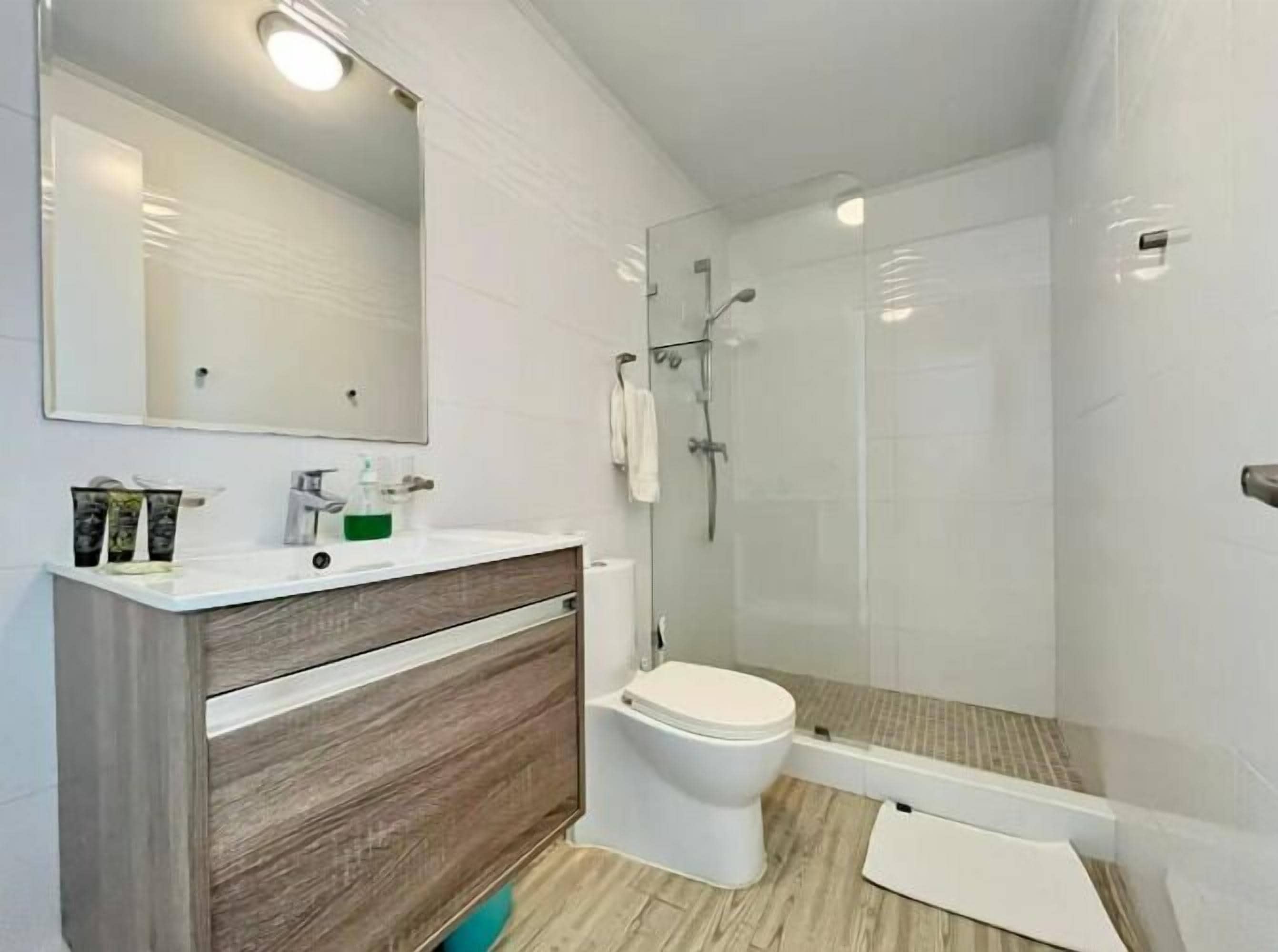 A modern bathroom with a wooden vanity, a large mirror, a toilet, and a glass-enclosed shower area.