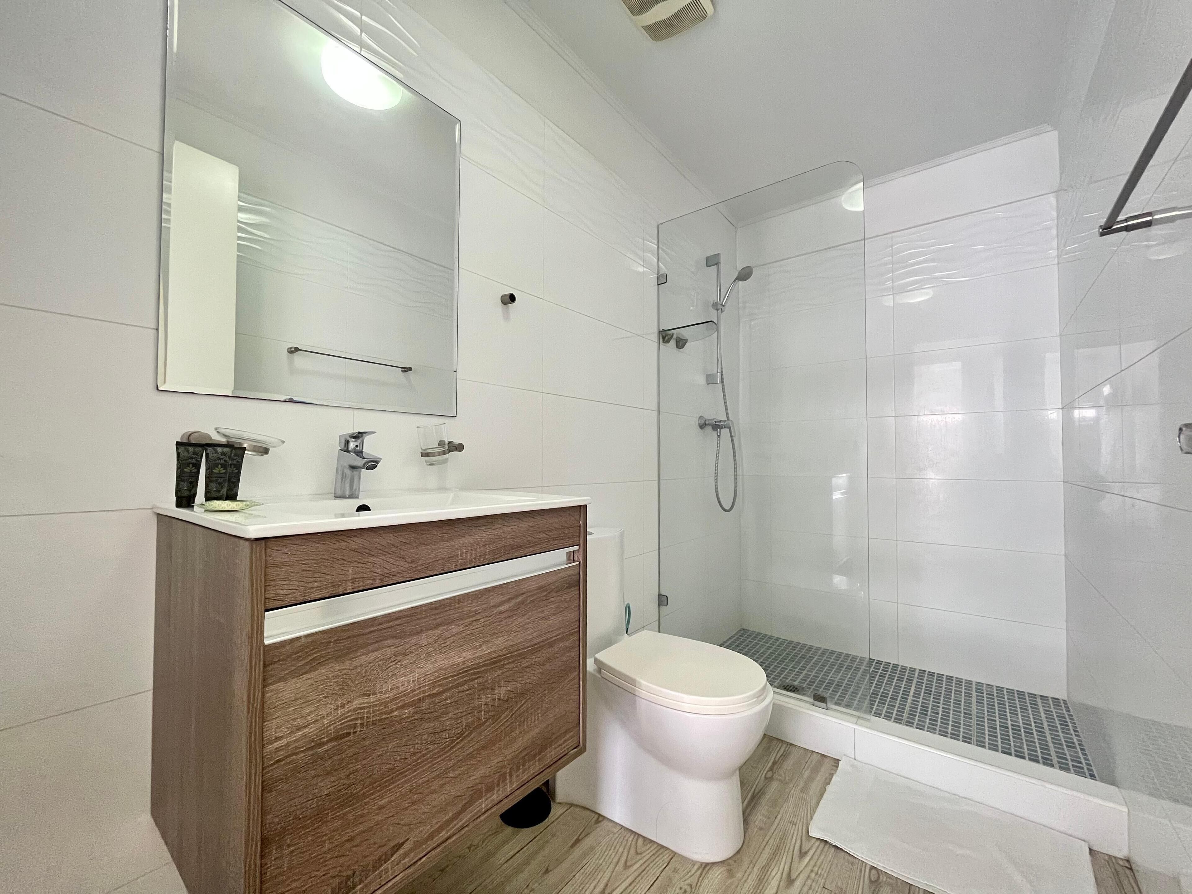A modern bathroom with a wooden vanity, a toilet, a glass shower enclosure, and a large mirror.