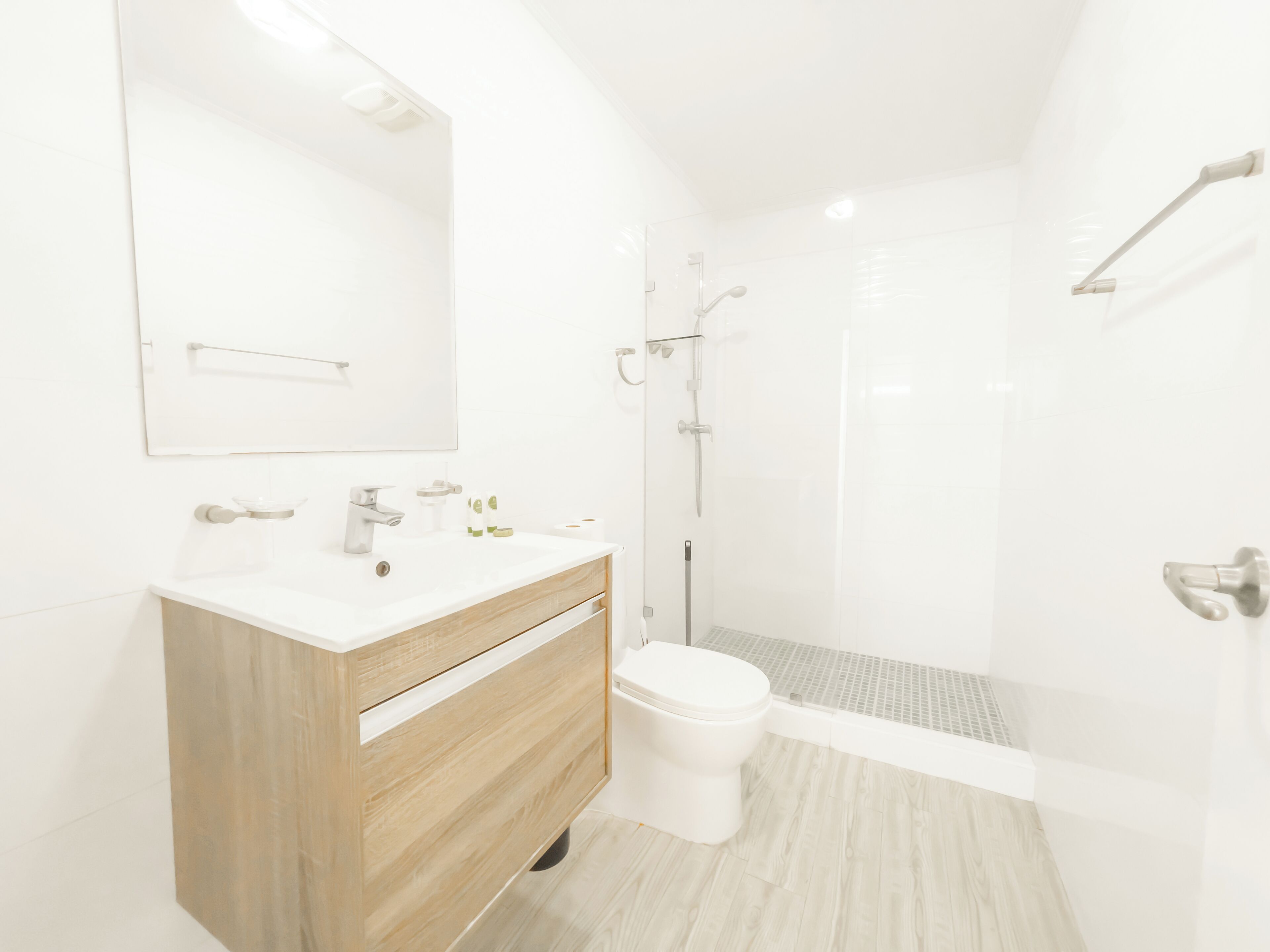 Un baño moderno con tocador de madera, inodoro blanco y cabina de ducha con mampara de vidrio.