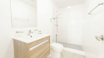 Un baño moderno con tocador de madera, inodoro blanco y cabina de ducha con mampara de vidrio.
