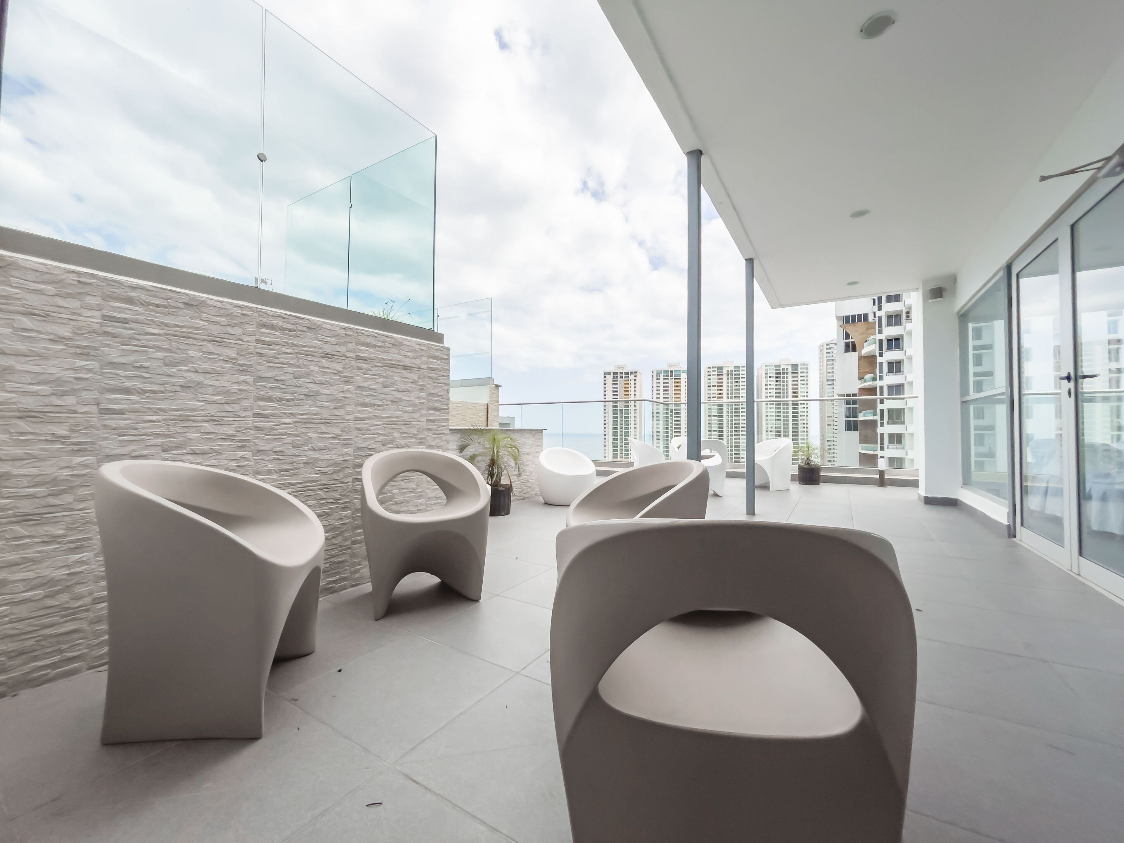 Un balcón moderno con mobiliario minimalista, una pared de piedra y vistas a edificios altos.