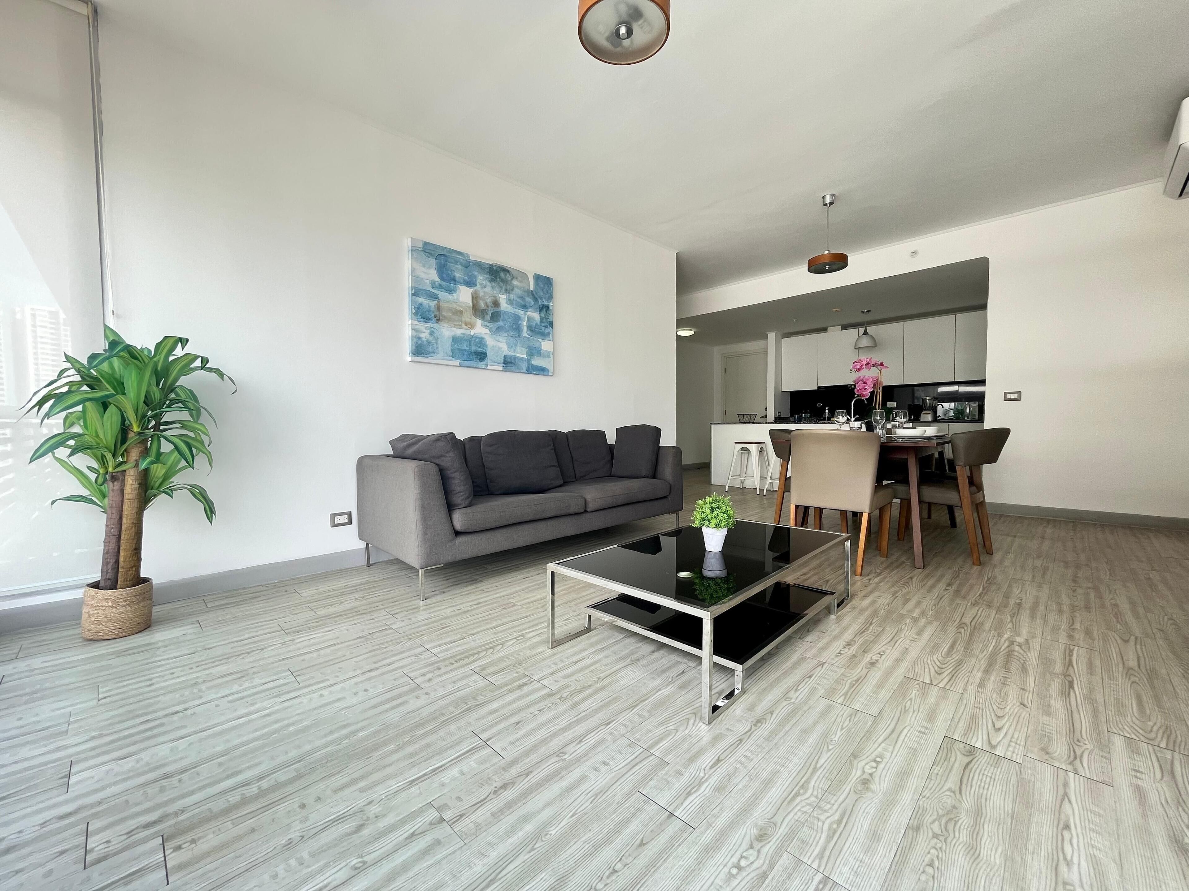 A modern living room with a grey sofa, a coffee table, and a potted plant.