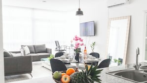 Una sala moderna con un sofá gris, una mesa de comedor preparada para cuatro personas y una cocina con lavaplatos y encimera.