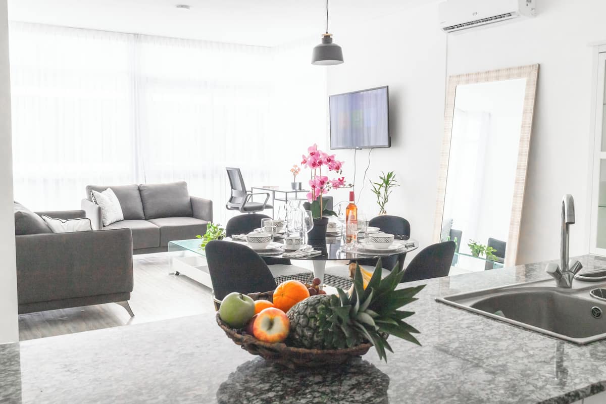 A modern living room with a grey sofa, a dining table set for four, and a kitchen area with a sink and countertop.