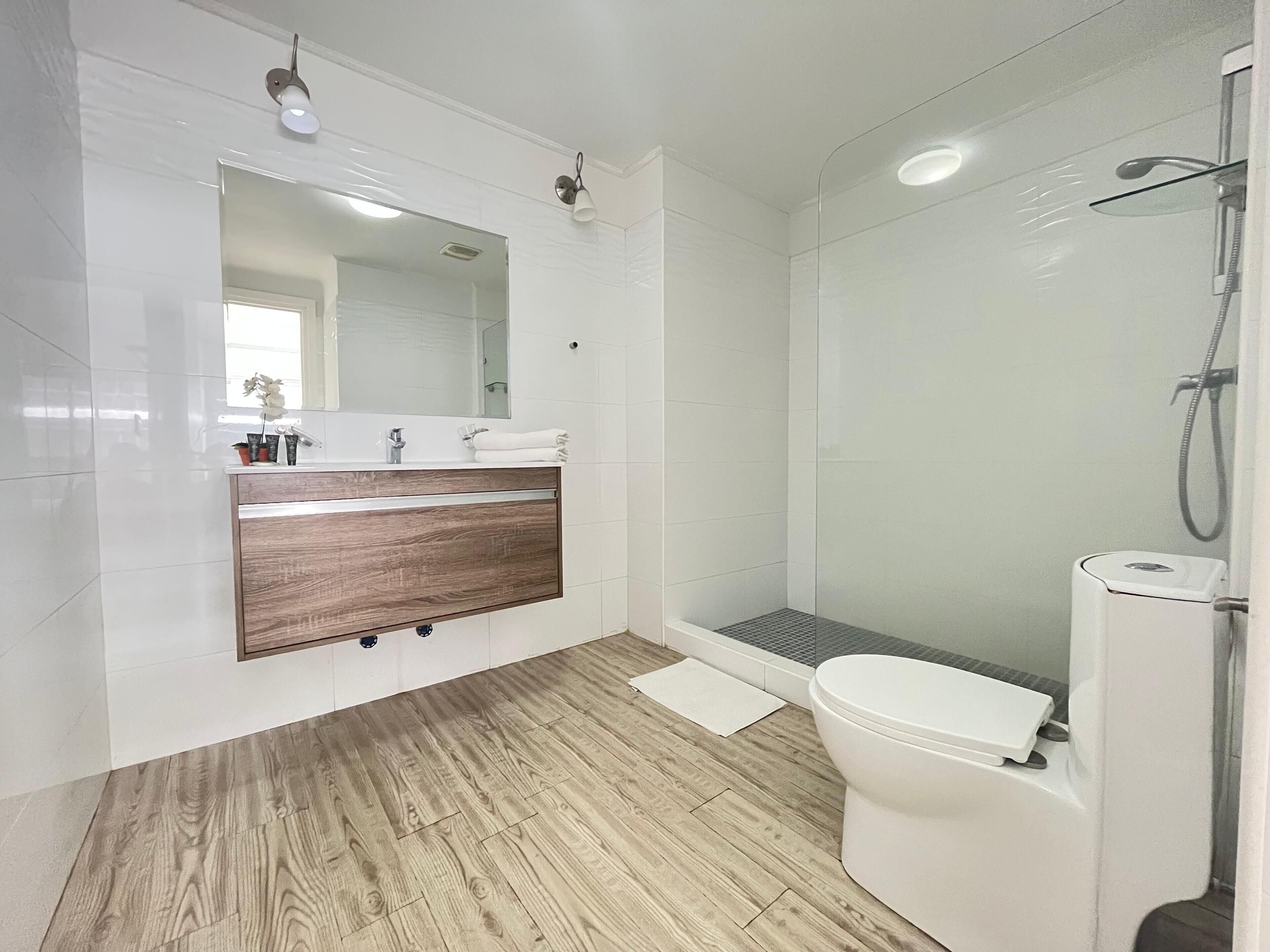 Une salle de bain moderne avec un meuble-lavabo en bois, un grand miroir, une cabine de douche et des toilettes.