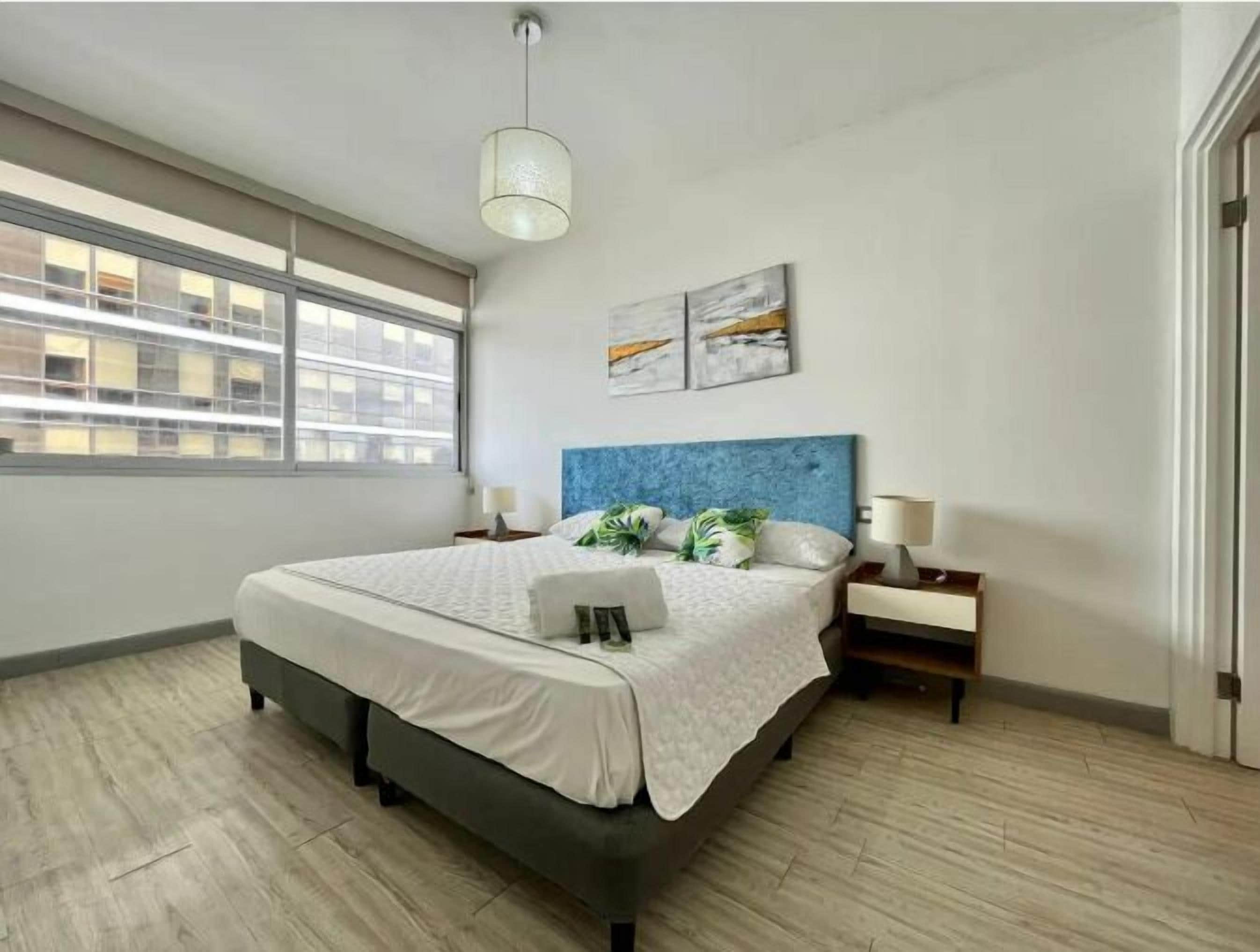 A modern bedroom with a large bed, a blue headboard, and artwork on the wall.