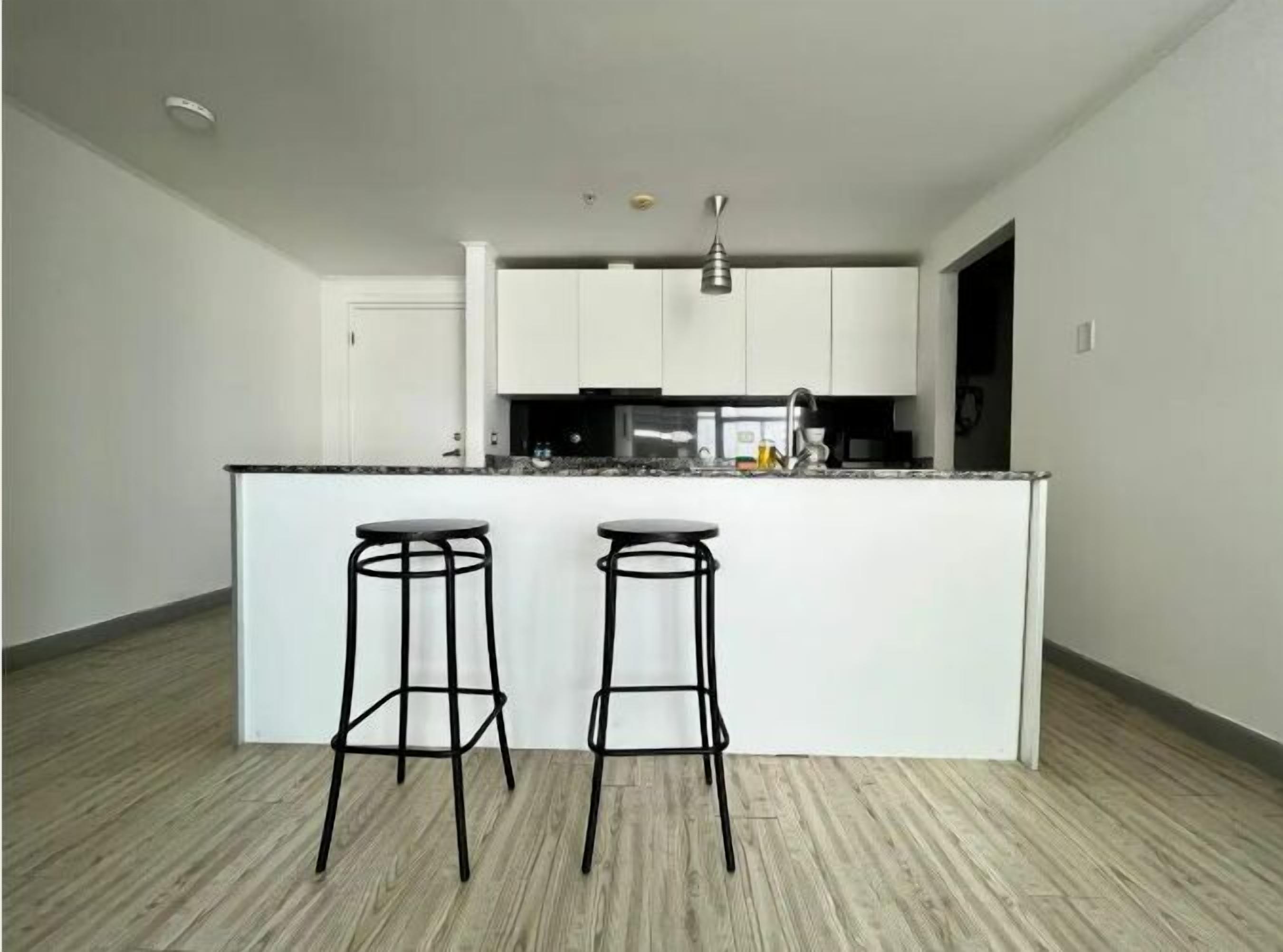 A modern kitchen with a central island, two bar stools, and white cabinetry.