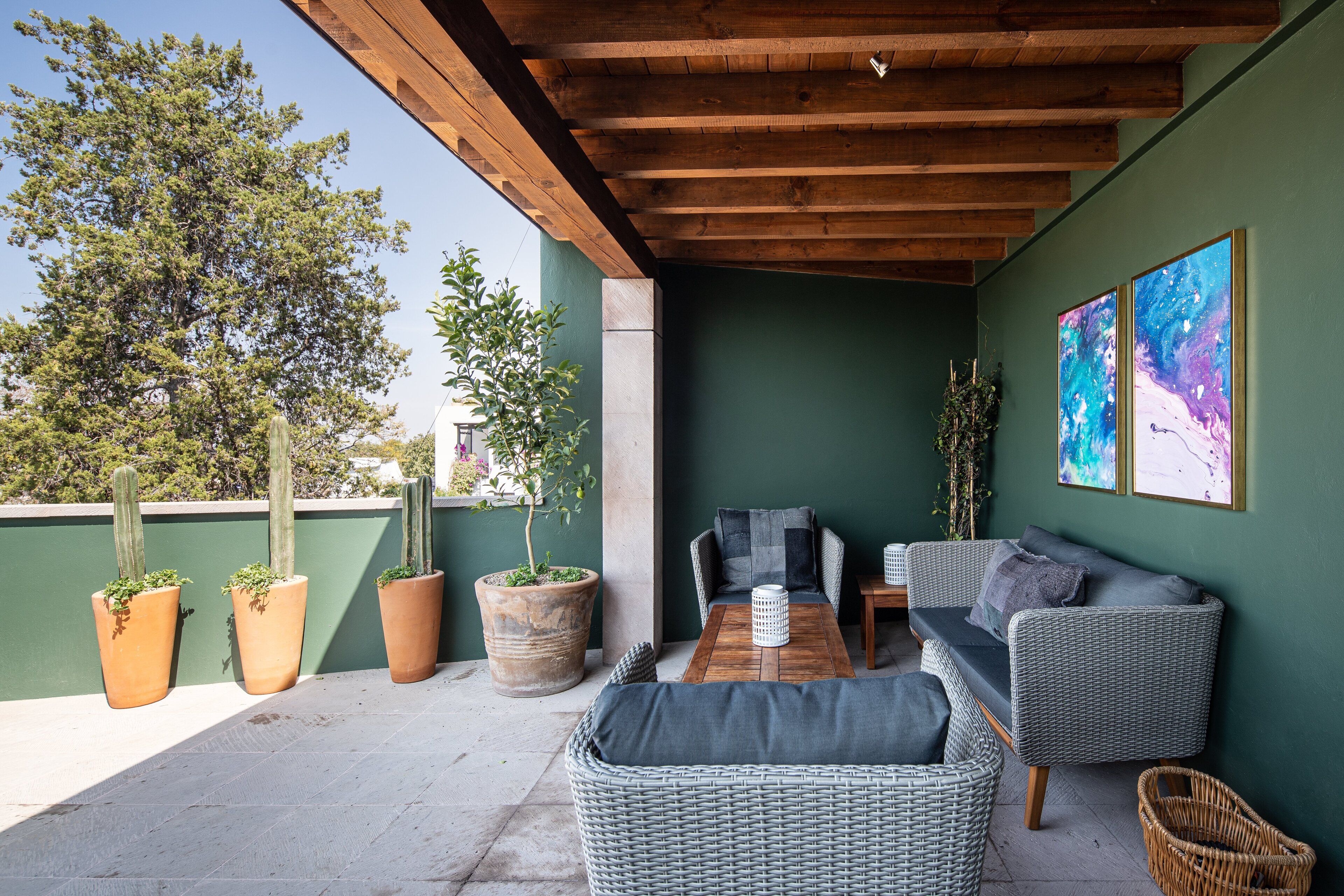 Une terrasse couverte, aménagée avec des meubles en osier, une table en bois et des plantes en pot.