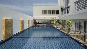 Une piscine intérieure moderne offrant une vue dégagée sur l’ensemble de l’espace piscine, ainsi qu’un coin salon et un bâtiment doté d’un balcon.
