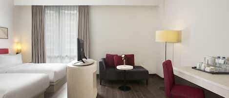 Una habitación de hotel con dos camas, un escritorio con lámpara, una silla y una televisión.