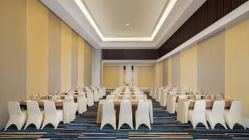 Un salón de conferencias con filas de mesas y sillas, una alfombra estampada y una paleta de colores neutros.
