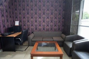 Una habitació amb un sofà, una taula de cafè, un escriptori amb un ordinador i un paper pintat amb motius.