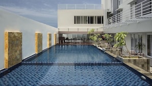Une piscine intérieure moderne offrant une vue dégagée sur l’ensemble de l’espace piscine, ainsi qu’un coin salon et un bâtiment doté d’un balcon.