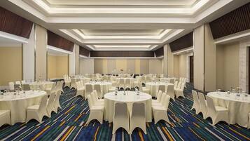 A conference room with multiple round tables, white chairs, and a patterned carpet.
