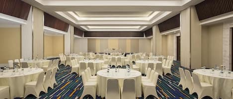 Un salón de conferencias con varias mesas redondas, sillas blancas y una alfombra estampada.