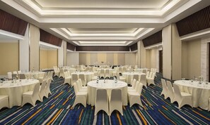 Un salón de conferencias con varias mesas redondas, sillas blancas y una alfombra estampada.