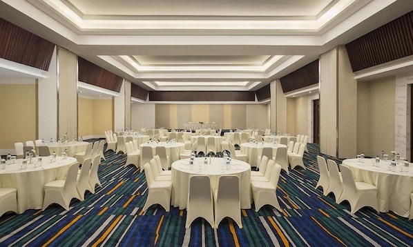 A conference room with multiple round tables, white chairs, and a patterned carpet.