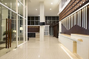 Um saguão de hotel moderno com balcão de recepção, portas de vidro e uma parede decorativa.