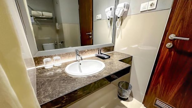 Une salle de bain avec un comptoir en marbre, un lavabo, un miroir, un porte-serviettes et une porte dotée d’une poignée.