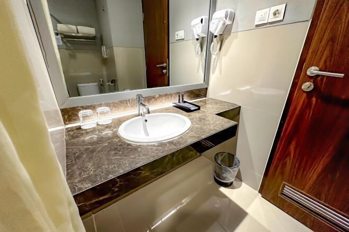Un baño con encimera de mármol, un lavabo, un espejo, un perchero para toallas y una puerta con manija.