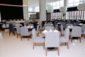 Un comedor moderno con sillas tapizadas en gris, vajilla blanca y amplios ventanales.