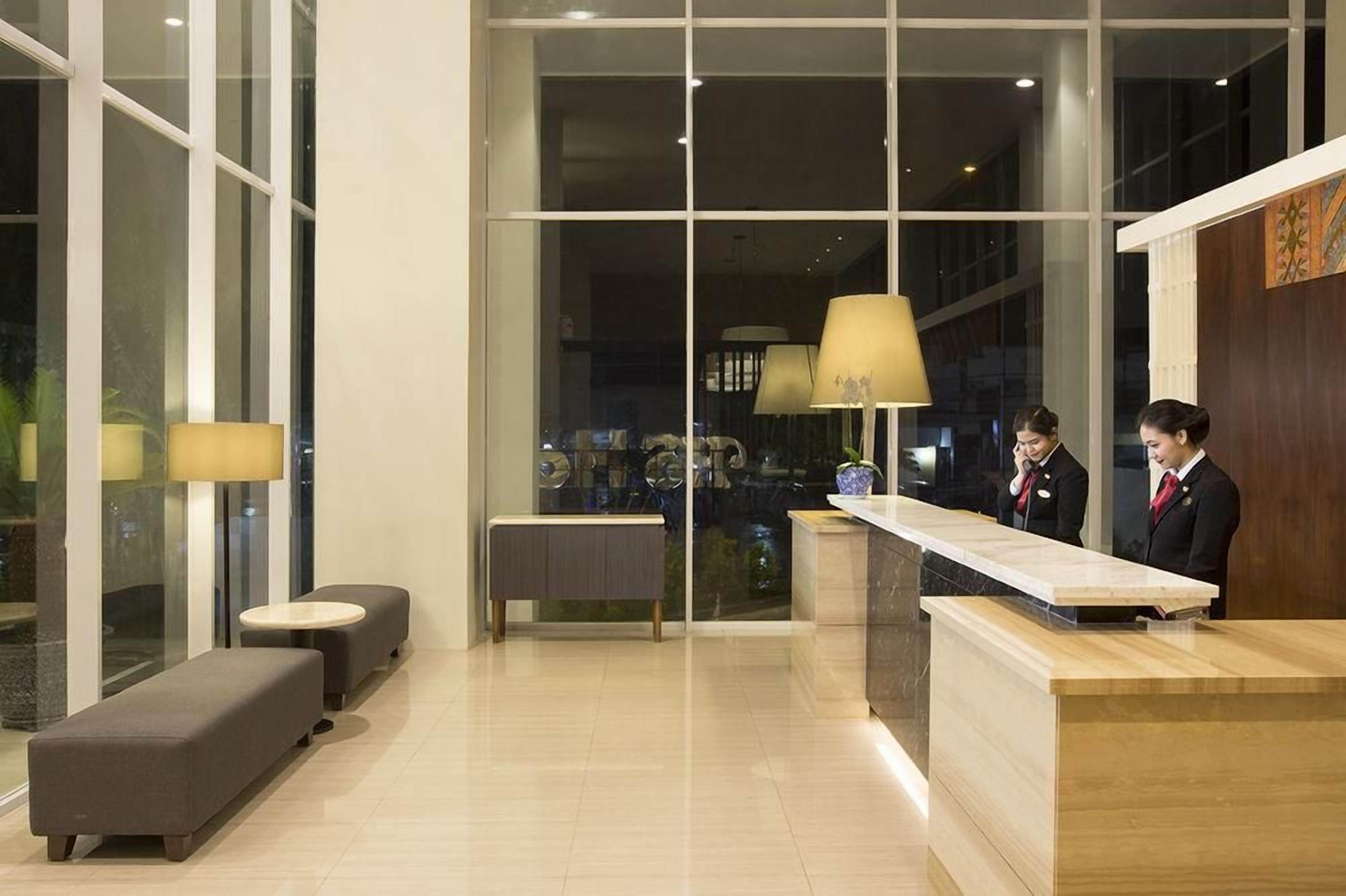 Zona de recepción de un hotel, con un mostrador, dos áreas de espera con sofás y un ventanal que ofrece vistas del interior.