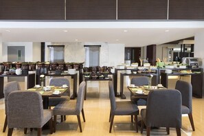 A modern dining area with multiple tables and chairs, kitchen appliances, and potted plants. - Howard Johnson by Wyndham Pekalongan Indonesia (Pekalongan)