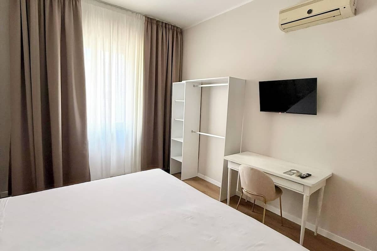 Una habitación de hotel con cama, escritorio, silla, armario, televisión de pantalla plana y aire acondicionado.