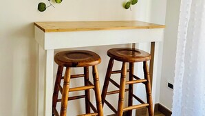 A white desk with two wooden stools, a mirror with a wooden frame, and green leafy vines. - Porta Amari (Palermo)