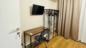 A room with a wooden desk, a chair, a TV mounted on the wall, a coat rack, and a window with curtains. - Porta Amari (Palermo)