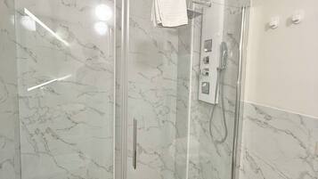 Un baño moderno con ducha envuelta en vidrio, paredes de mármol y un perchero para toallas.
