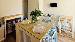 A modern kitchen with a central island, wooden stools, a potted plant, and a built-in storage unit. - Porta Amari (Palermo)