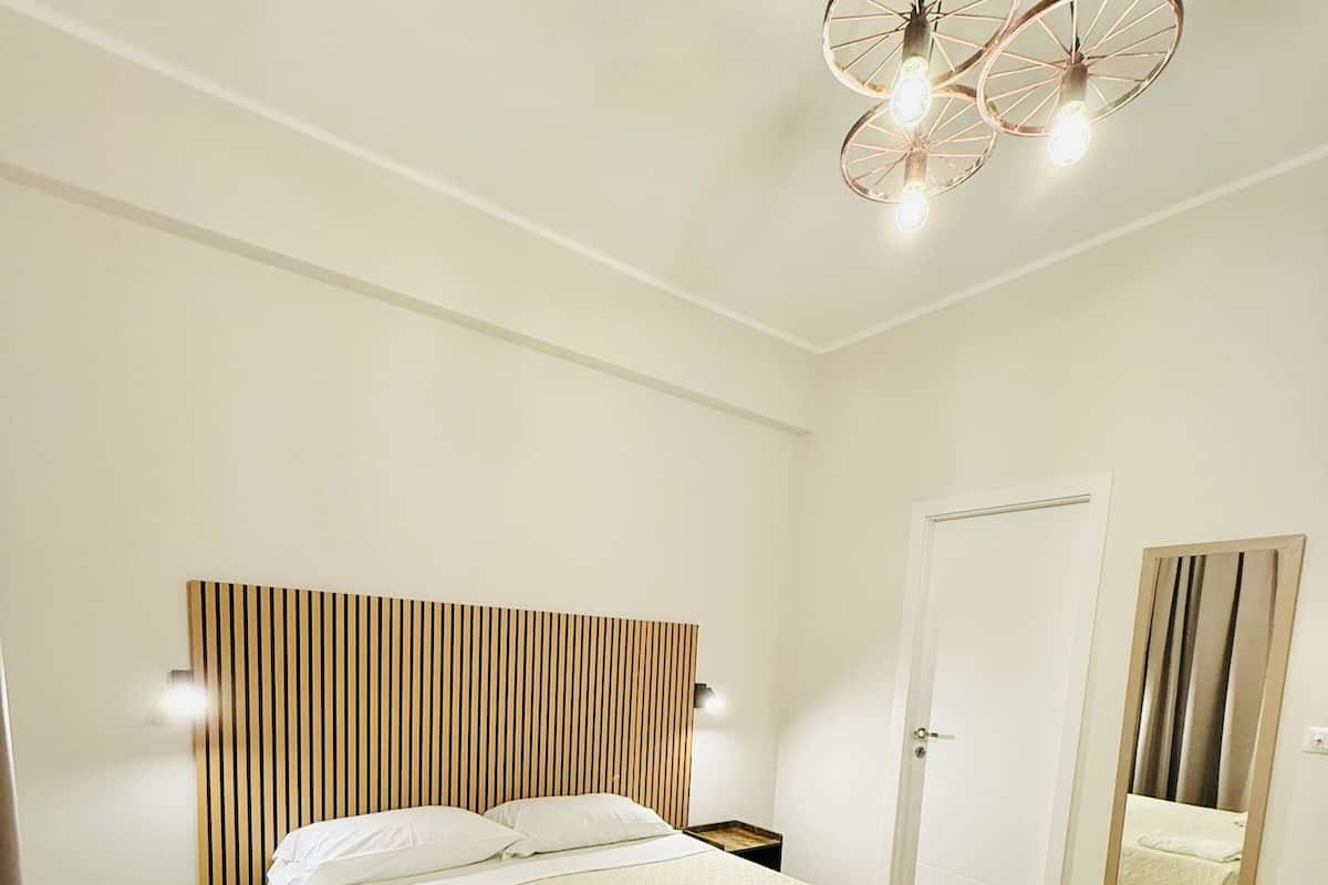 Un dormitorio moderno con cama, mesitas de noche, cabecera de madera, espejo y una lámpara de techo original.