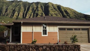 A single-story house with a garage, a stone retaining wall, and a mountain in the background. - Family Friendly 3BR w/Mt views, Close to Beach (Waianae)
