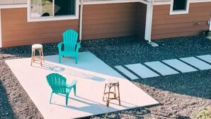 A house with a covered patio area featuring two green Adirondack chairs and a wooden stool. - Family Friendly 3BR w/Mt views, Close to Beach (Waianae)