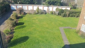 A well-maintained grassy yard with a brick building, a paved driveway, and a garage with white doors. - Luxurious Living in the Heart of Bromley (Bromley)