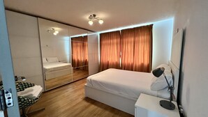 A modern hotel room with a large bed, a bedside table with a lamp, a mirror, and a seating area with a chair and a small table. - Luxurious Living in the Heart of Bromley (Bromley)