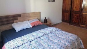 A bedroom with a wooden headboard, a bed with patterned bedding, a nightstand with a lamp, and a wardrobe. - A beautiful apartment with traditional architecture 3 minutes from bouregreg (Salé)
