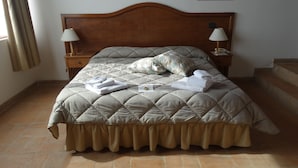 Una cama bien hecha con una colcha acolchada, dos lámparas de noche y una toalla doblada sobre la mesita de noche.