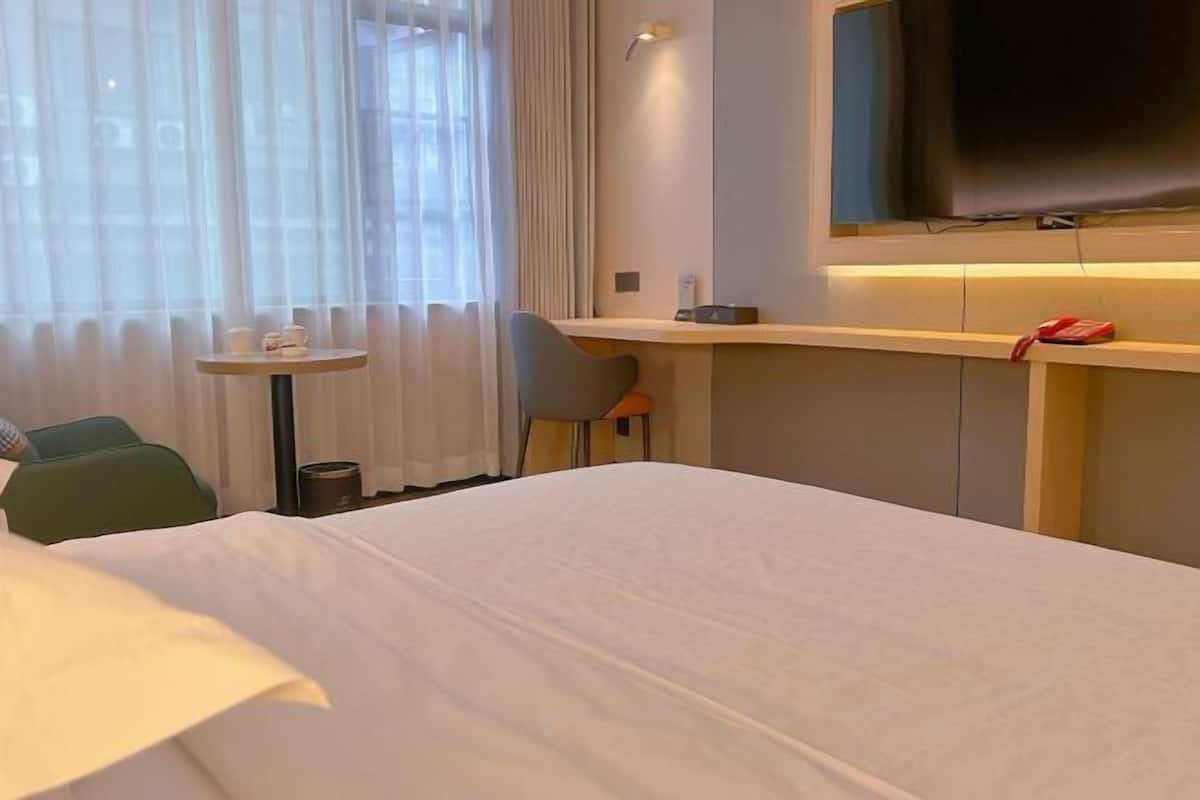 Ein Hotelzimmer mit Bett, Schreibtisch, Stuhl, Fernseher und einem Fenster mit Vorhängen.