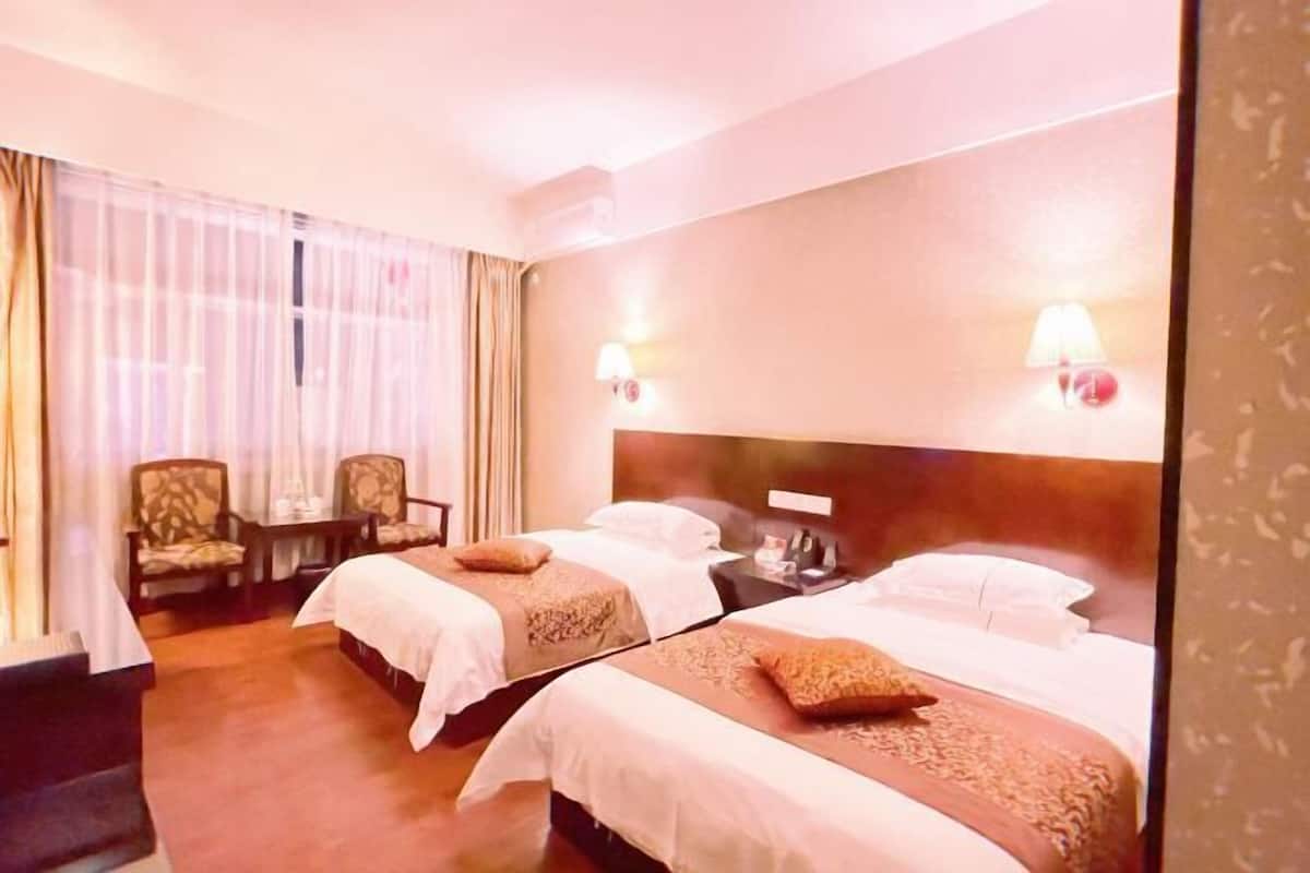 Ein Hotelzimmer mit zwei Betten, einem Schreibtisch, einem Stuhl und einem Fenster mit Vorhängen.