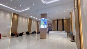 Een ruime lobby met een modern design, met een receptiebalie, een zithoek en een digitale informatiezuil.