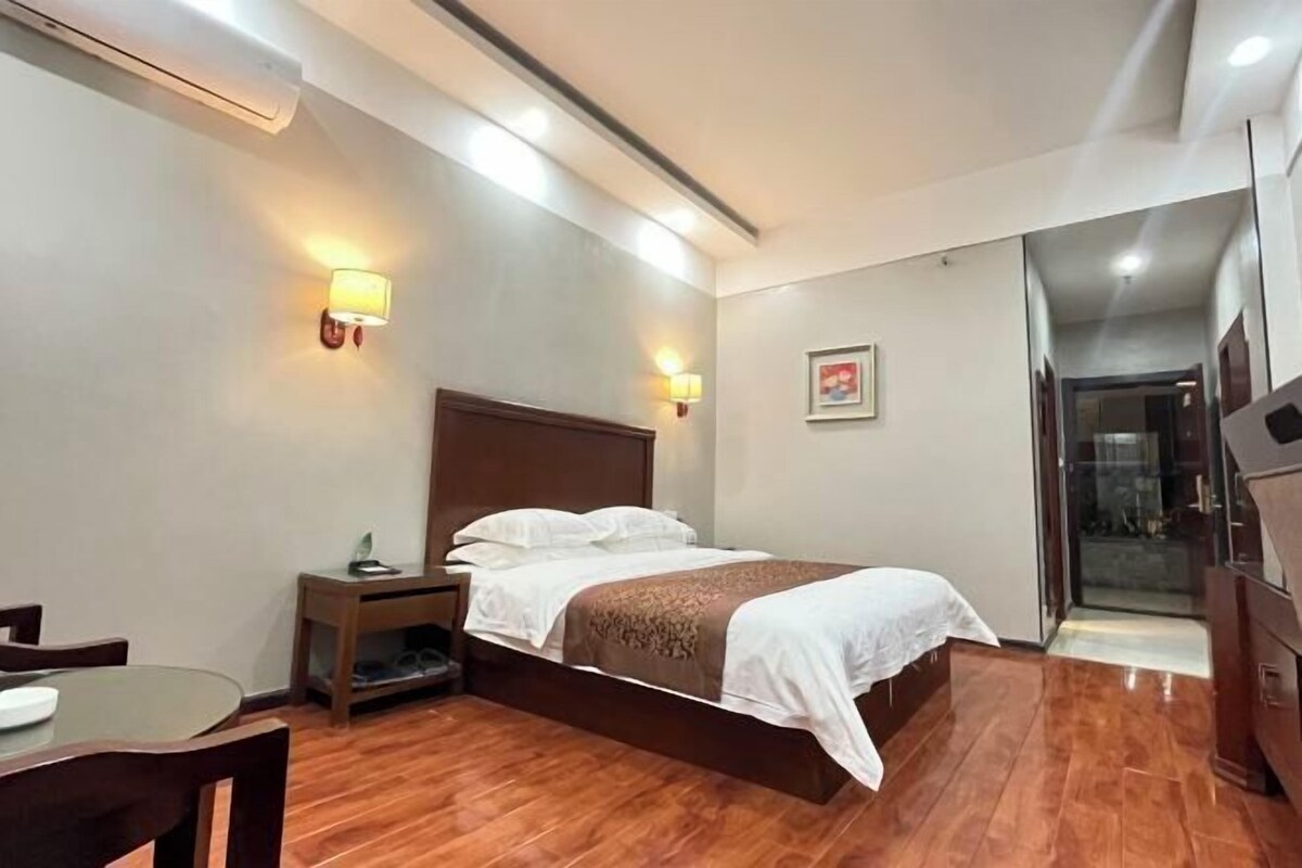 Une chambre d’hôtel avec un plancher en bois, un lit avec du linge de lit blanc, une table de chevet avec une lampe et une petite table avec une chaise.