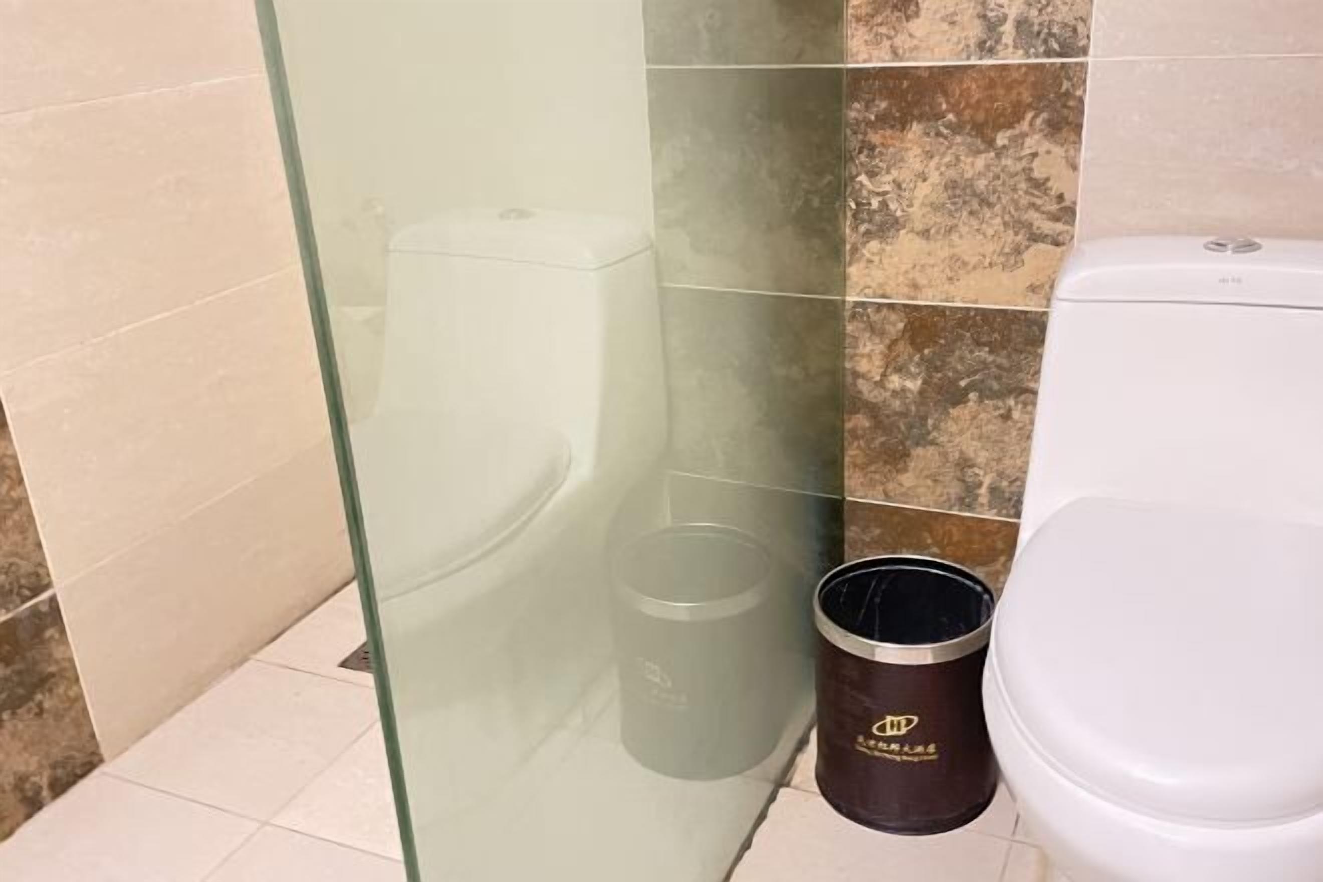 Baño con cabina de ducha de vidrio, inodoro y cubo de basura.