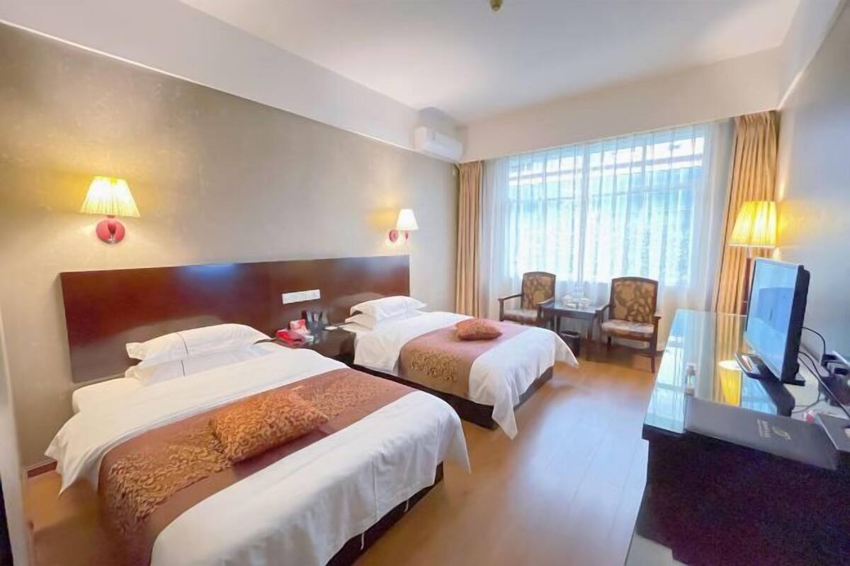 Ein Hotelzimmer mit zwei Betten, einem Schreibtisch mit Computer, einem Stuhl und einem Fernseher.