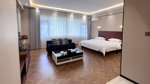 Een hotelkamer met een bed, een slaapbank, een salontafel, een spiegel en een raam met gordijnen.
