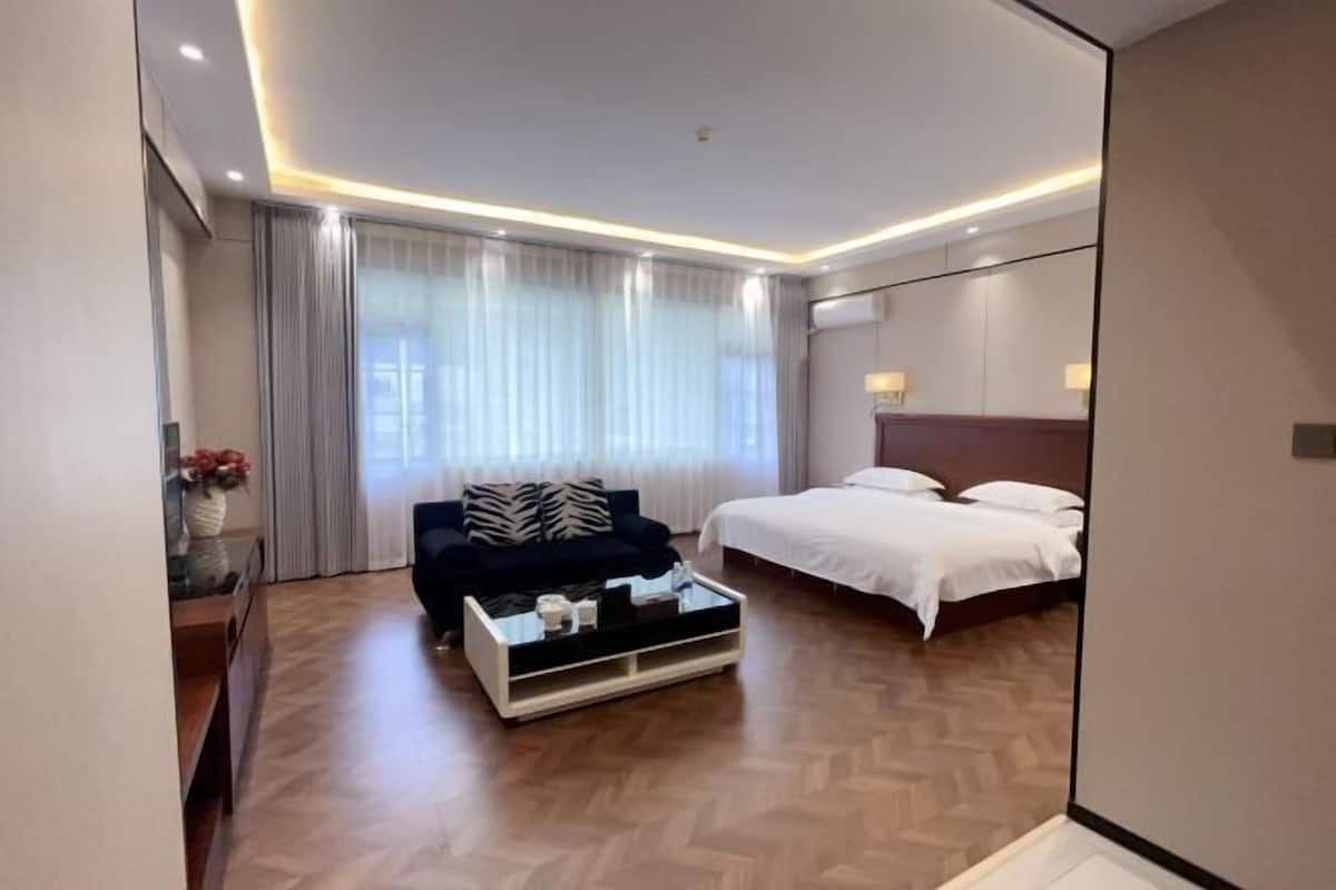 Ein Hotelzimmer mit Bett, Sofa, Couchtisch, Spiegel und einem Fenster mit Vorhängen.