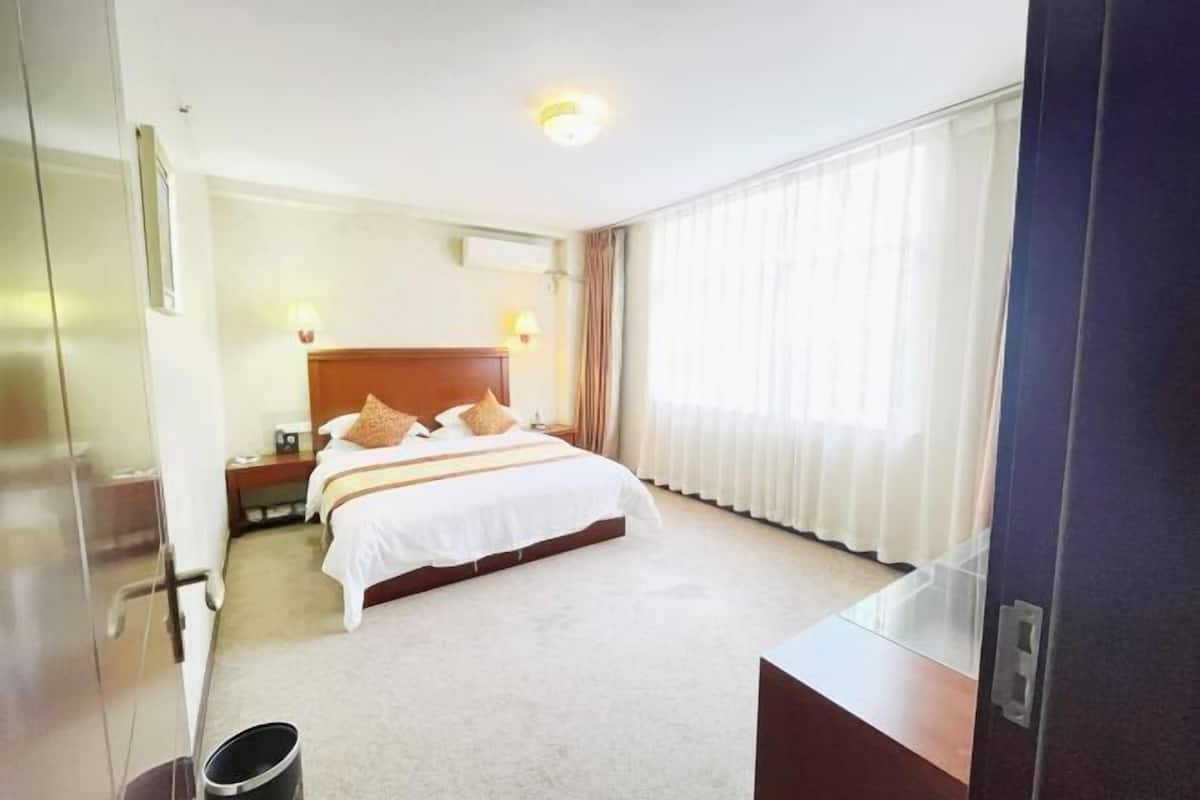 Ein Hotelzimmer mit einem großen Bett, einem Nachttisch, einer Lampe und einem Fenster mit Vorhängen.